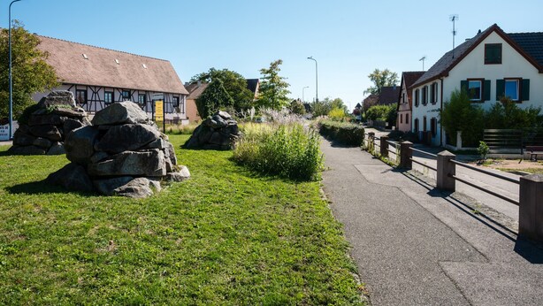 Ein traditionelles europäisches Dorf mit Steinhäusern, einem gepflasterten Weg und viel Grün.