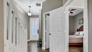 A hallway with a wooden floor, white doors, a ceiling fan, and a bed with a wooden headboard in the adjacent room.