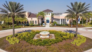 A hotel entrance with a central fountain, palm trees, and a clear sky. - Modern 7BR Villa | Pool + Resort Amenities (Kissimmee)