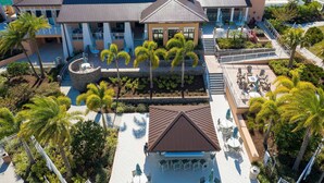 An aerial view of a hotel with a central courtyard, palm trees, outdoor seating, and a covered patio area. - Modern 7BR Villa | Pool + Resort Amenities (Kissimmee)