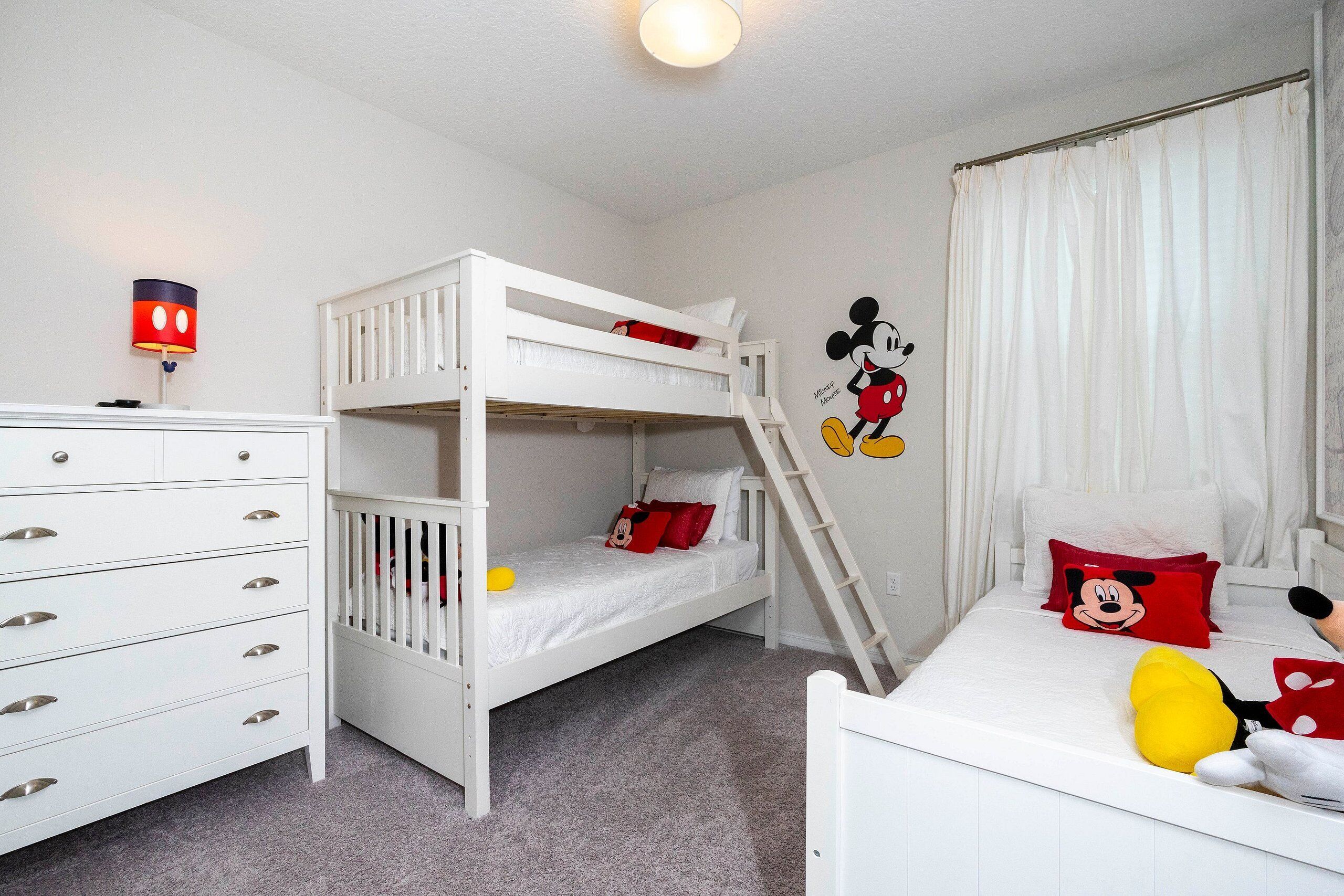 A bunk bed room with a white dresser, Mickey Mouse wall decal, and a window with white curtains.