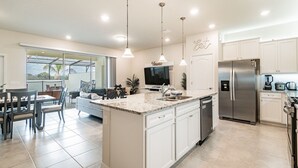 A modern kitchen with white cabinets, a stainless steel refrigerator, and a large island with a sink. - 5B/4.5B Pool and Resort (Davenport)