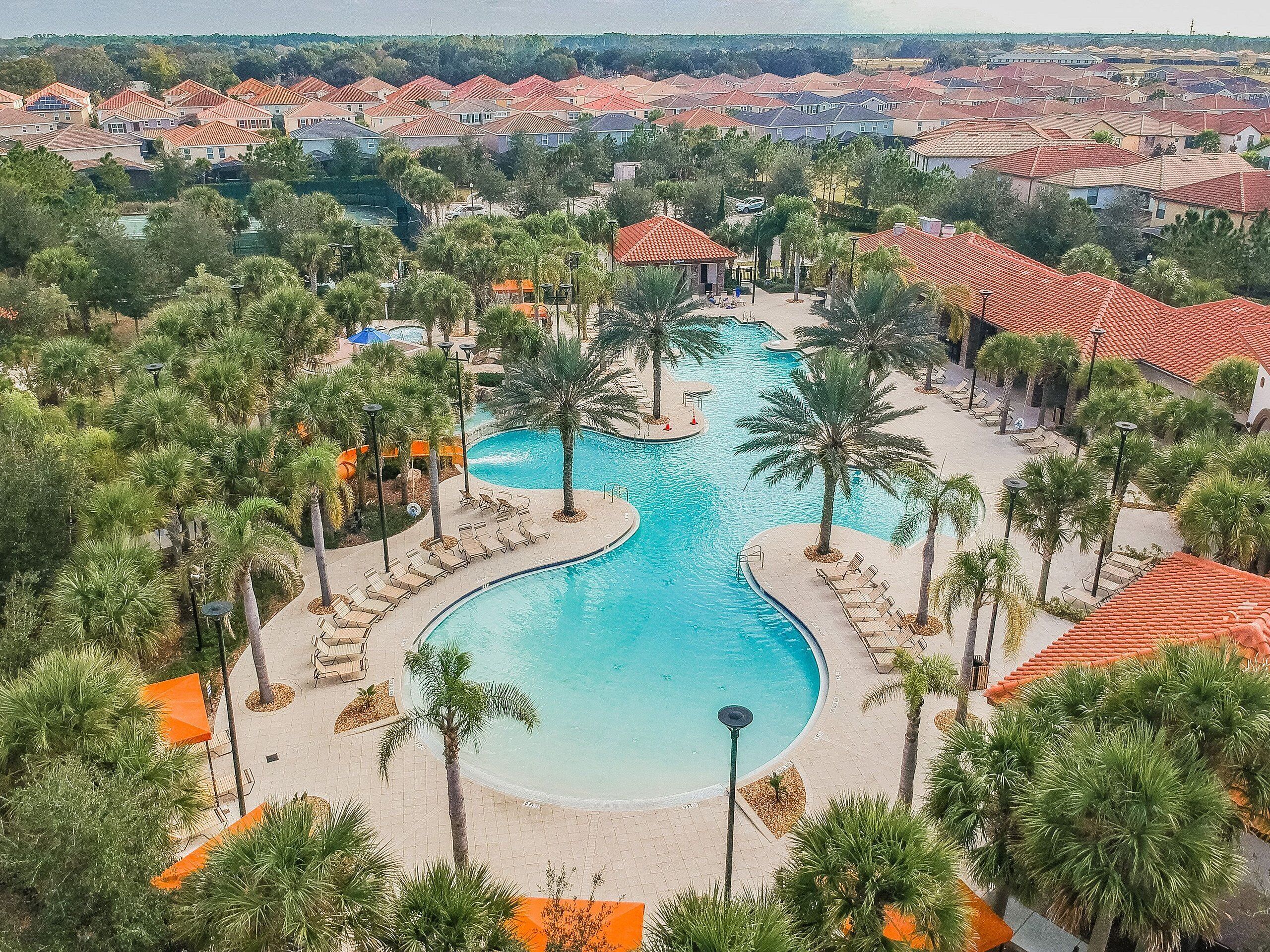 A resort with a large central pool, surrounded by palm trees and lounge chairs.
