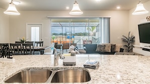 A modern kitchen with a large island, stainless steel sink, and pendant lighting. - 5B/4.5B Pool and Resort (Davenport)