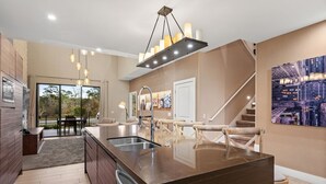 Una cocina moderna con una isla central, iluminación colgante y una escalera que lleva a otro nivel.