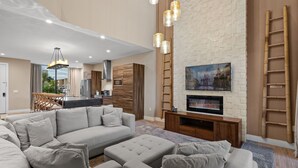 Una sala de estar moderna con un sofá modular, un televisor de pantalla plana montado en una pared de ladrillo y una cocina al fondo.