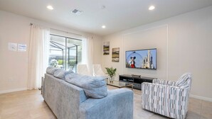 Una sala moderna con un sofá gris, un sillón estampado, un televisor de pantalla plana y una mesa de centro de vidrio.