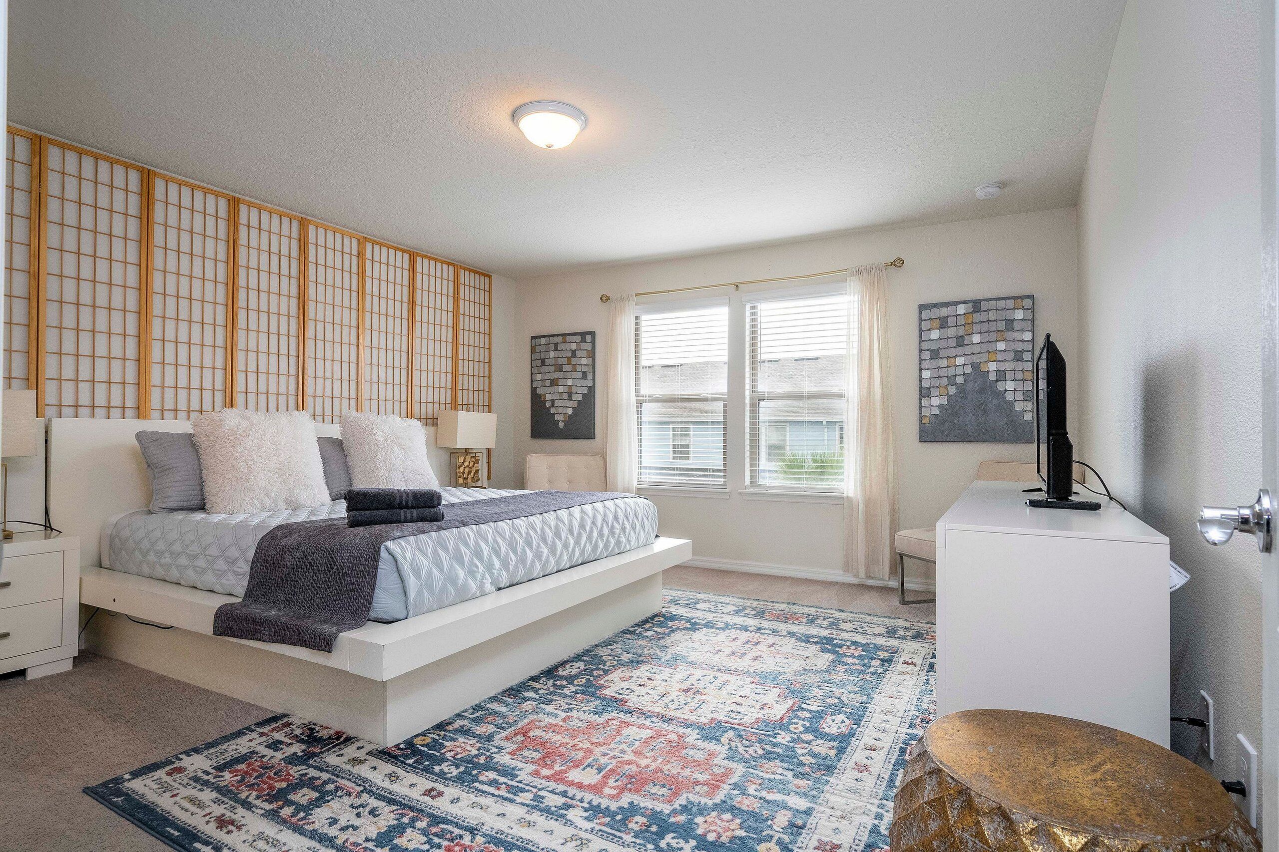 A bedroom with a bed, bedside tables, a desk, a chair, and a window with blinds.