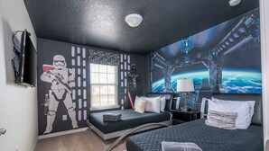 Un dormitorio con dos camas, decoración de Star Wars en la pared, una ventana y vistas de la Tierra desde el espacio.