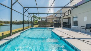 A swimming pool with a covered patio area, a view of a lake, and outdoor furniture. - 5BR Lake Berkley Home, Lake-View Pool (Kissimmee)