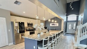 A modern kitchen with a central island, bar stools, stainless steel appliances, and pendant lighting. - 5BR Lake Berkley Home, Lake-View Pool (Kissimmee)