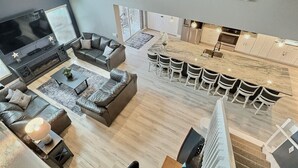 A modern living room with a large TV, leather sofas, and a dining area with bar stools. - 5BR Lake Berkley Home, Lake-View Pool (Kissimmee)