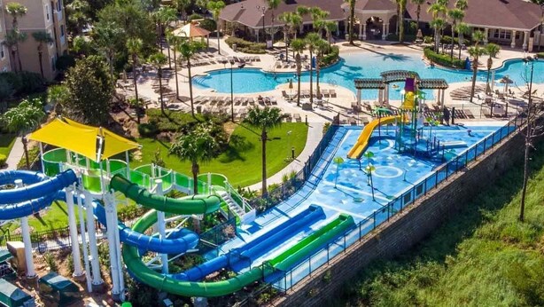 Parque acuático con toboganes y piscinas múltiples, rodeado de palmeras y un edificio de hotel.