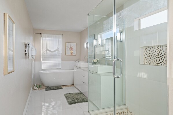 A modern bathroom with a glass-enclosed shower, a freestanding bathtub, and a vanity with a mirror.