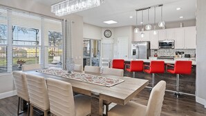 Una cocina moderna con armarios blancos, un refrigerador de acero inoxidable y un comedor con mesa de madera y sillas color beige.
