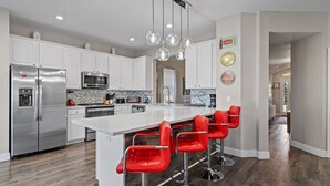 Una cocina moderna con armarios blancos, electrodomésticos de acero inoxidable y una isla central con taburetes rojos.