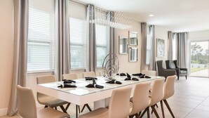 A modern dining area with a glass table, beige chairs, and a chandelier.