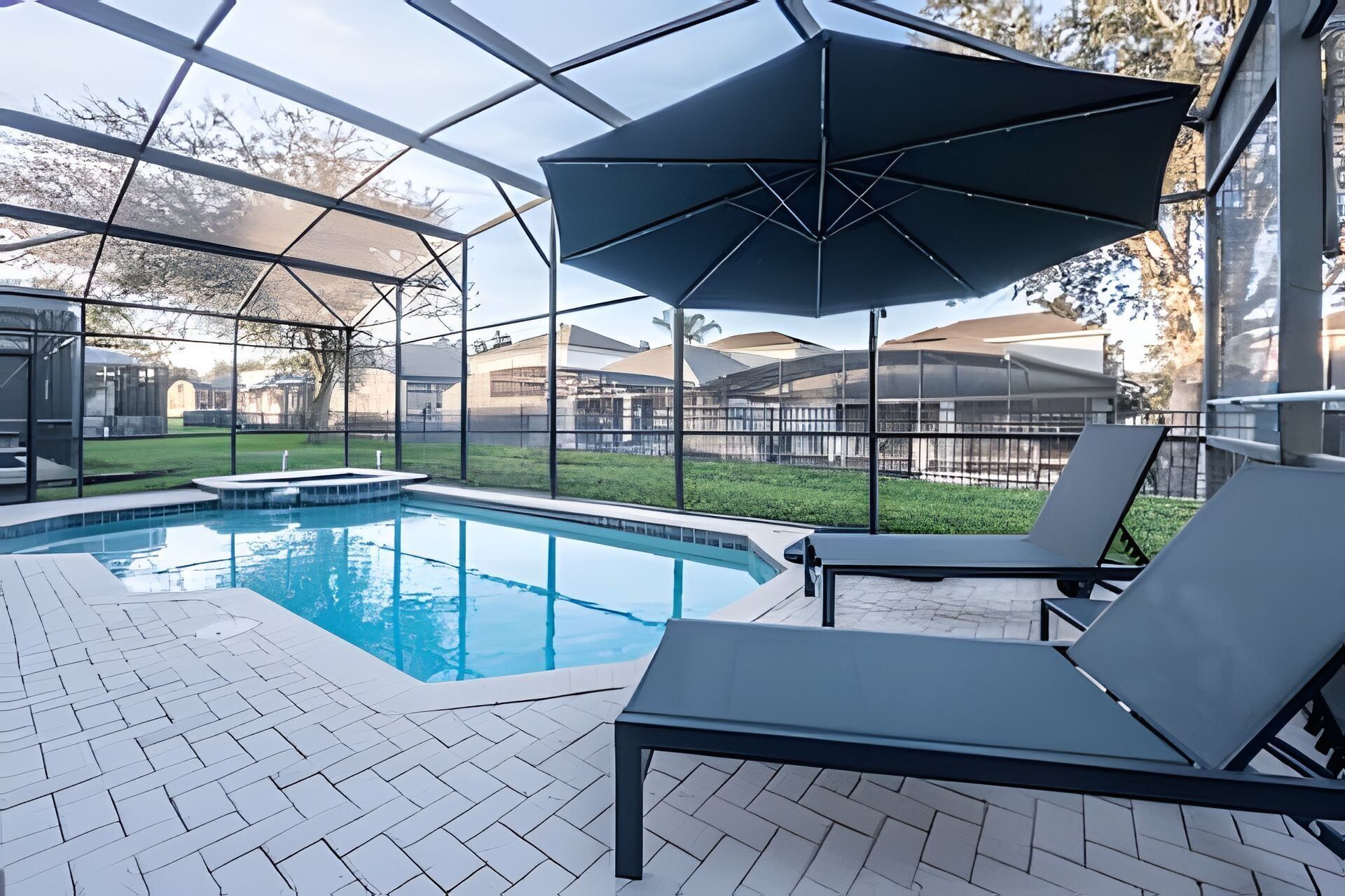 A swimming pool with a glass enclosure, lounge chairs, and a large umbrella.