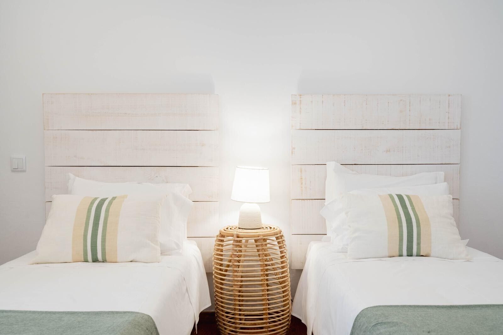 Ein Zimmer mit zwei Betten, einem gewebten Nachttisch und einer Wandlampe.