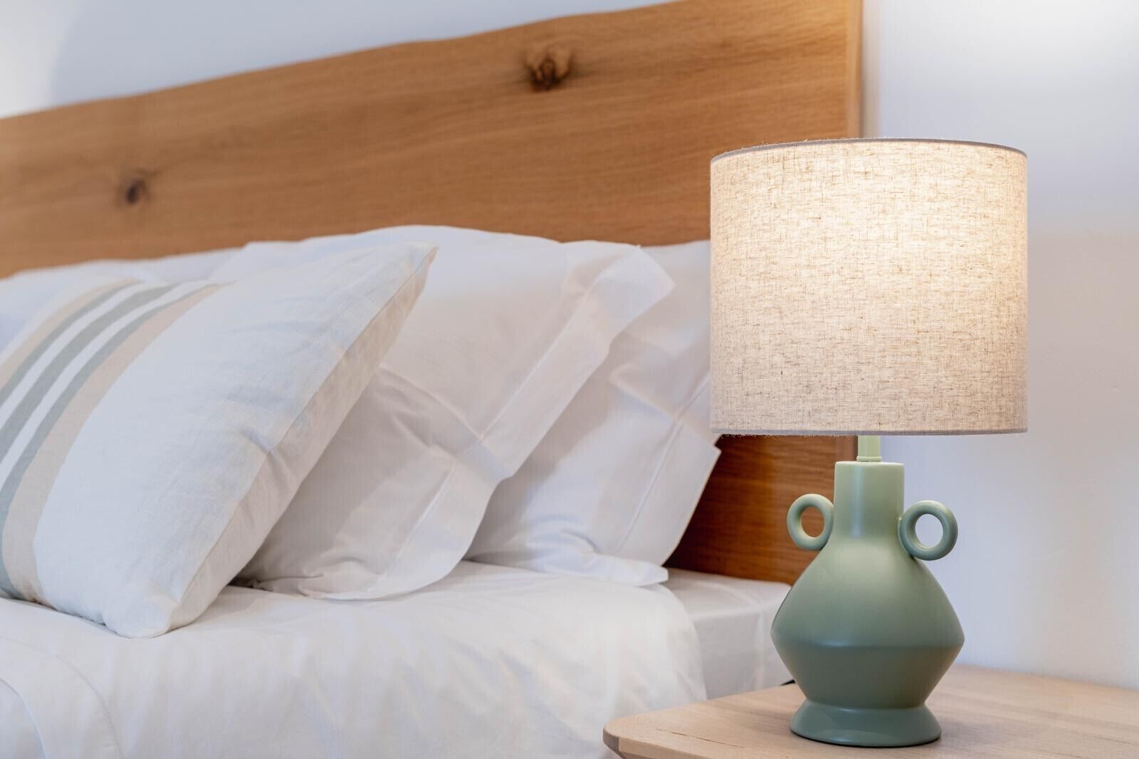 A bed with white bedding and a green lamp on a wooden nightstand.