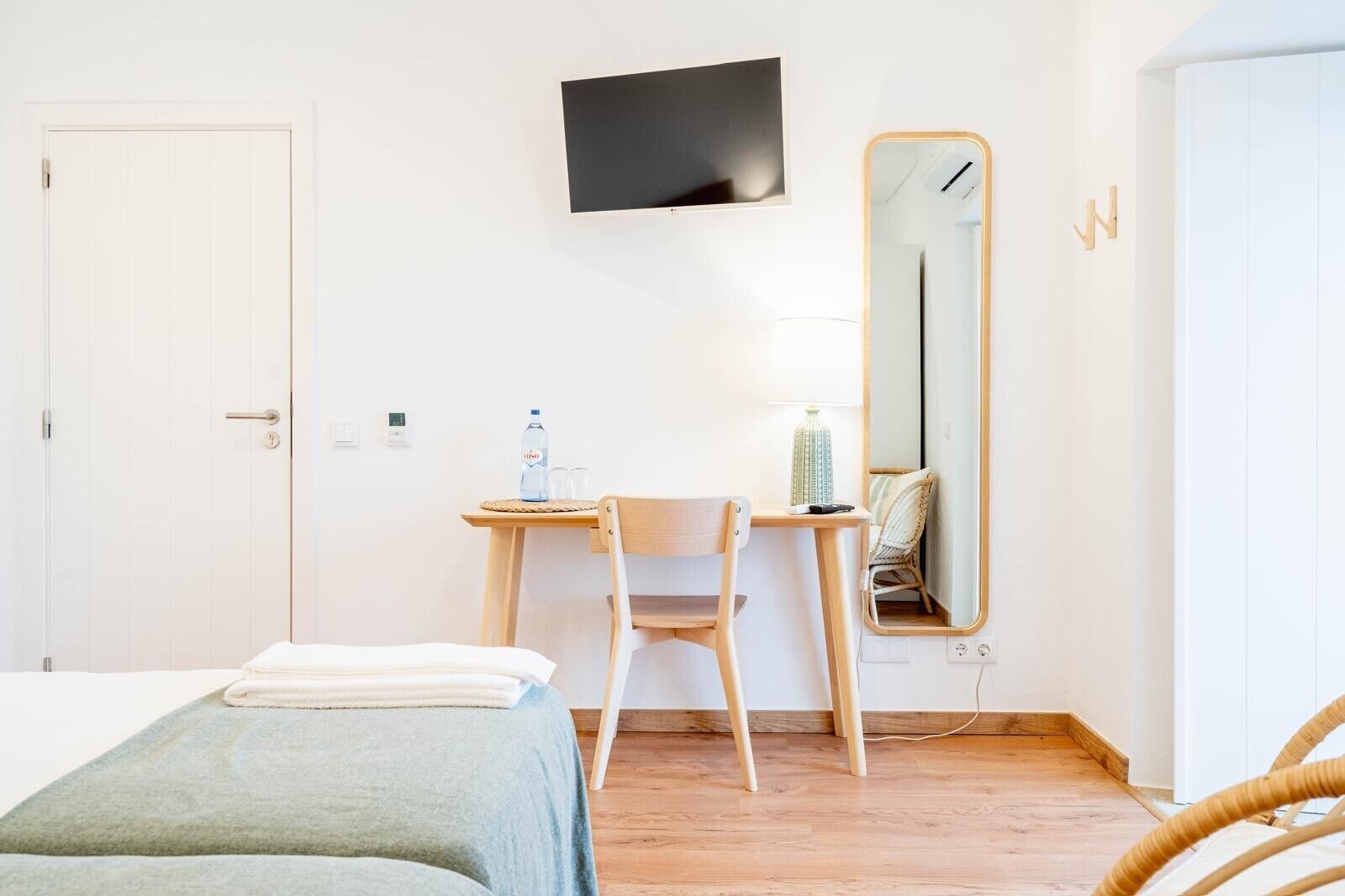 A hotel room with a bed, a desk with a chair, a TV mounted on the wall, and a mirror.