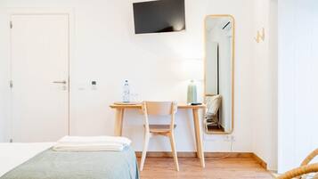 A hotel room with a bed, a desk with a chair, a TV mounted on the wall, and a mirror.