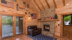 A log cabin interior with a stone fireplace, leather sofa, wooden floors, and American flags. - All Arrows Pointe To This Vacation Cabin (PIGEON FORGE)
