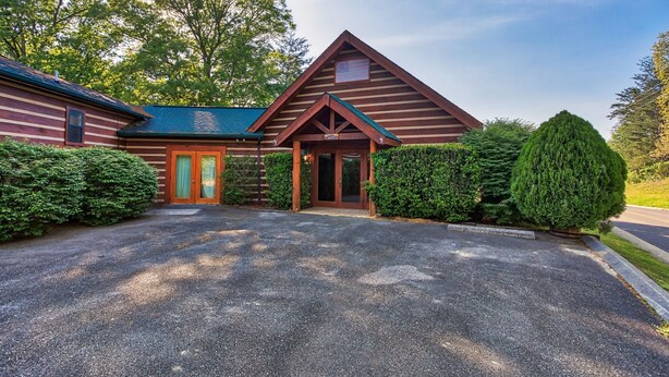 A log cabin with a front porch, a green roof, and a gravel driveway. - All Arrows Pointe To This Vacation Cabin (PIGEON FORGE)