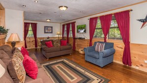 A cozy living room with a brown sofa, a blue armchair, and a wooden dining table. - All Arrows Pointe To This Vacation Cabin (PIGEON FORGE)