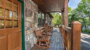 A wooden porch with rocking chairs and a stone wall. - All Arrows Pointe To This Vacation Cabin (PIGEON FORGE)