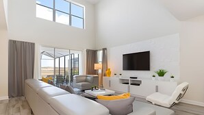 Een ruime woonkamer met een grote hoekbank, een flatscreen televisie aan de muur en een balkon met een glazen deur.