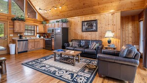 A spacious living area with a wooden ceiling, a large window, a fireplace, and a cozy seating arrangement.