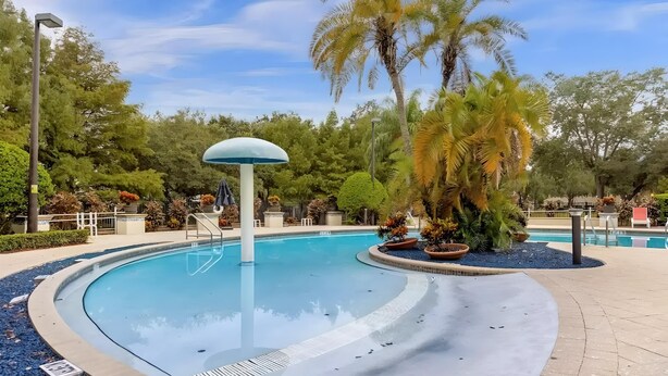 Una piscina con una fuente central, rodeada de palmeras y un paseo pavimentado.