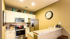 Una cocina moderna con armarios blancos, electrodomésticos de acero inoxidable, encimera de granito y un reloj en la pared.