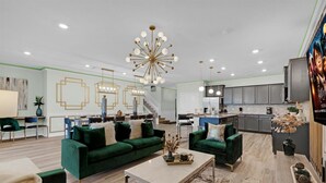 A spacious living room with green sofas, a coffee table, and a modern chandelier. - Mhd3074 (Davenport)