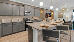 A modern kitchen with grey cabinets, a central island with bar stools, a built-in oven, and a large window. - Mhd3074 (Davenport)