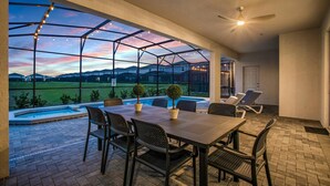 A covered patio with a pool, outdoor seating, and a view of a residential area at dusk. - Mhd3074 (Davenport)