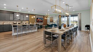 A modern kitchen with a central island, a dining area with a large table, and a living space with a TV. - Mhd3074 (Davenport)