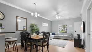 A modern living room with a grey sofa, a dining area with a wooden table and chairs, and a ceiling fan. - 3BR Home with Private Pool Near Disney (Kissimmee)