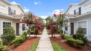 A residential street with two-story houses, a concrete pathway, and flowering plants. - 3BR Home with Private Pool Near Disney (Kissimmee)