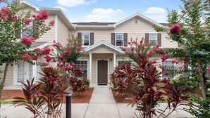 A two-story house with a front entrance, surrounded by a garden with flowering plants and shrubs. - 3BR Home with Private Pool Near Disney (Kissimmee)
