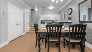 A modern kitchen with white cabinets, a microwave, and a refrigerator. There is a dining table with chairs and a chandelier above. - 3BR Home with Private Pool Near Disney (Kissimmee)
