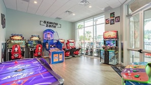 A gaming zone with various arcade machines, a pool table, and large windows offering a view of the outdoors.