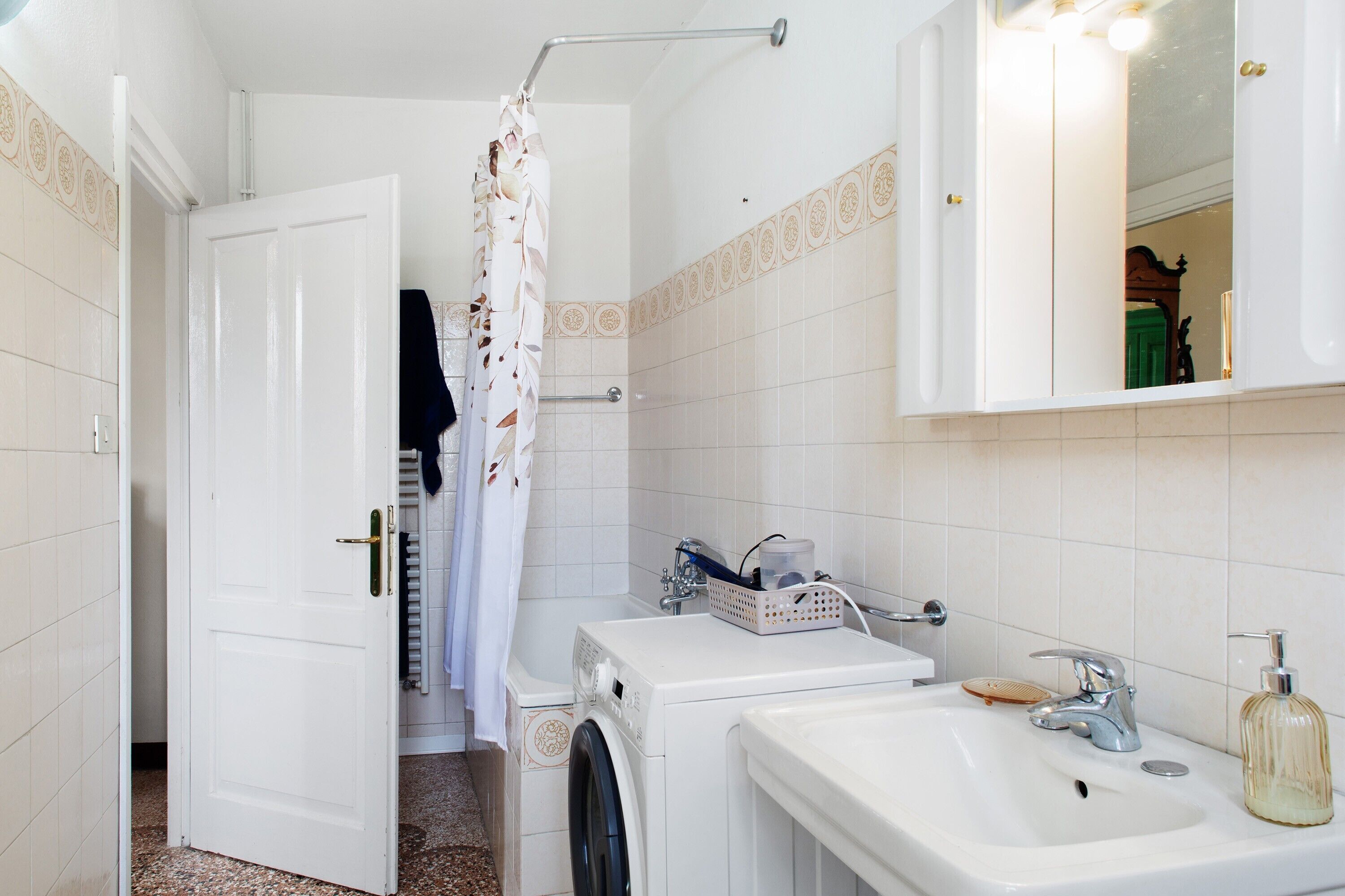 Un bagno con lavatrice, lavandino con dispenser di sapone e specchio.