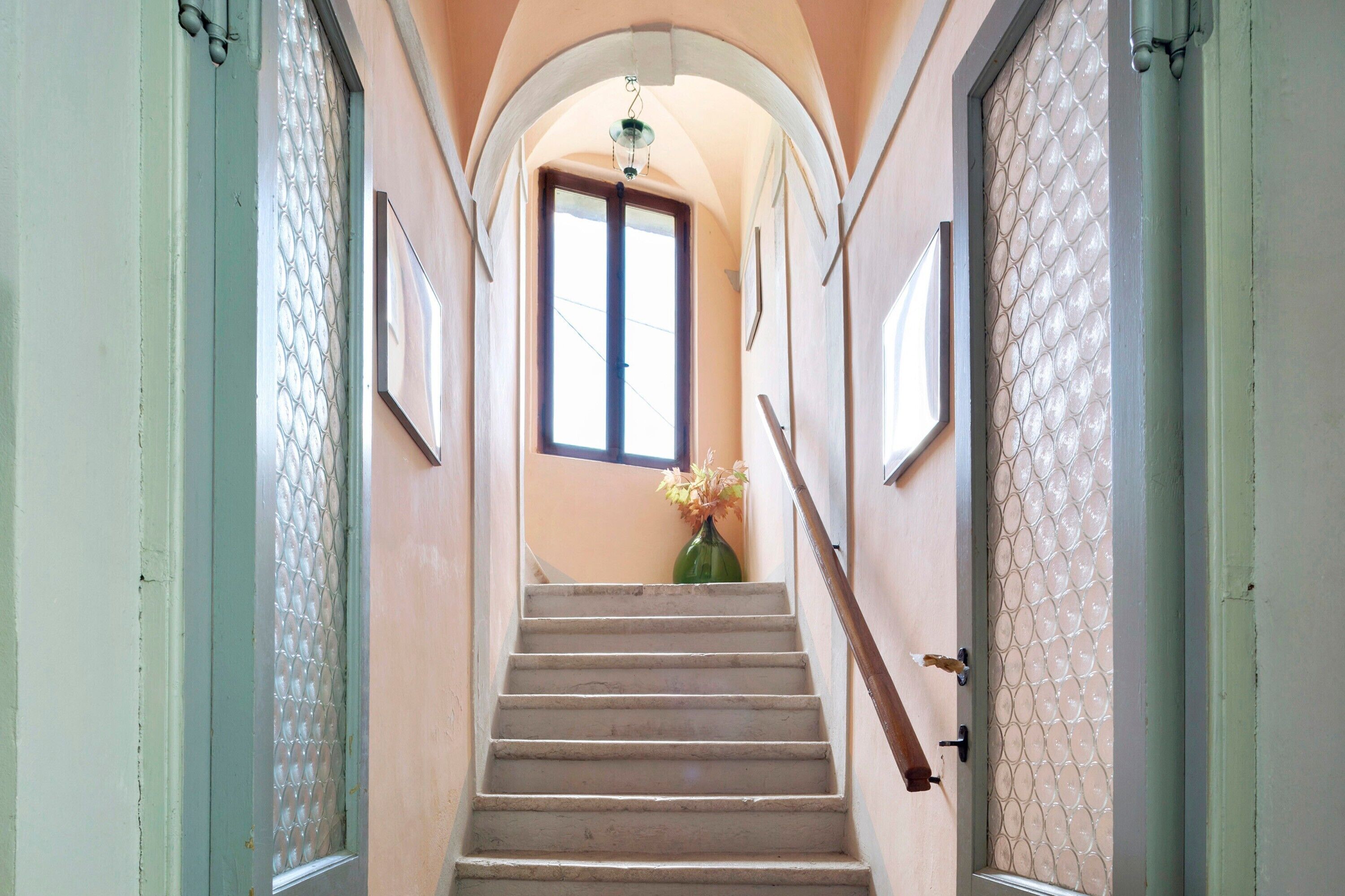 A staircase with a handrail, a window with a view, and a vase with flowers.