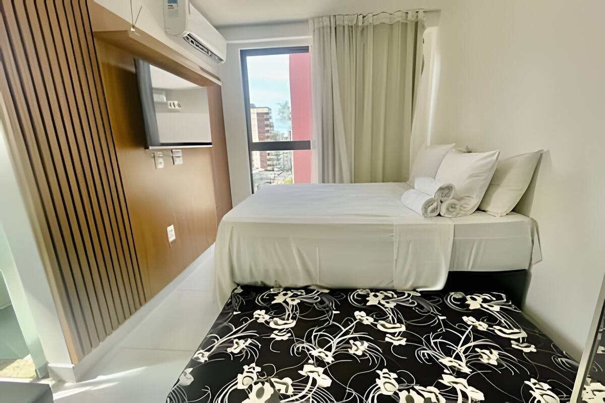 Une chambre d’hôtel avec un lit, un téléviseur fixé au mur et une fenêtre avec des rideaux.