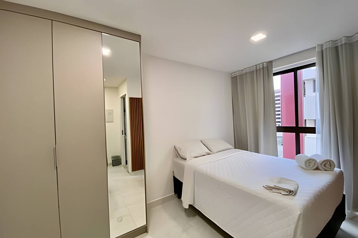 Une chambre d’hôtel avec un lit, un miroir, une fenêtre avec des rideaux et une vue sur l’extérieur.