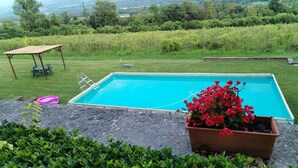 A rectangular swimming pool with a ladder, surrounded by a grassy area with a wooden table and chairs, and a potted plant with red flowers. - Apartment 'Bivai - Merlot' with Shared Pool, Private Terrace and Wi-Fi (Bivai)