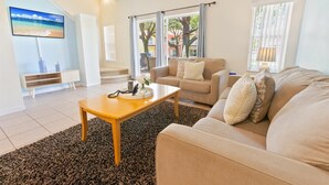 A living room with a beige sofa, a wooden coffee table, and a TV on the wall.