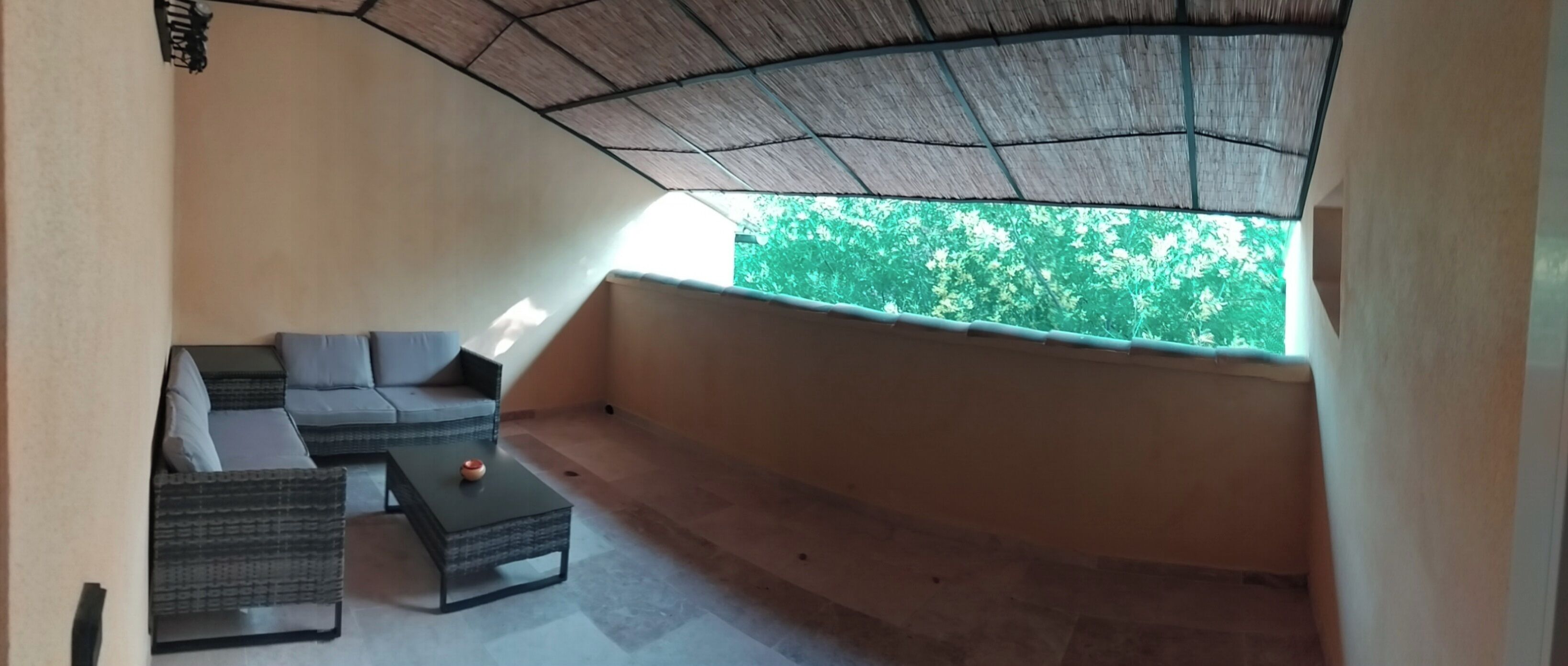 A balcony with a sofa, a small table, and a view of green trees.